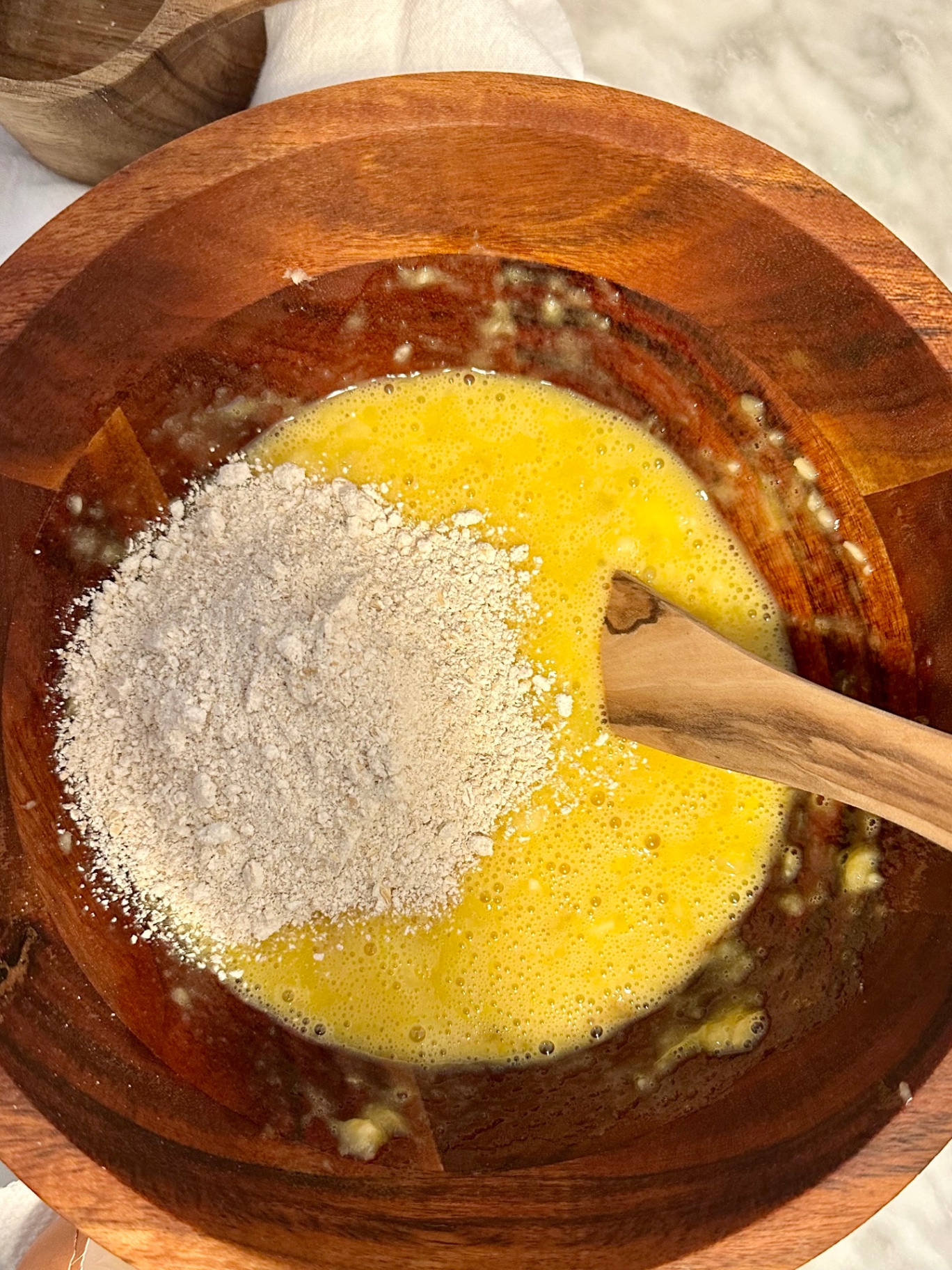 Oat flour being added to the wet ingredients in a wooden bowl