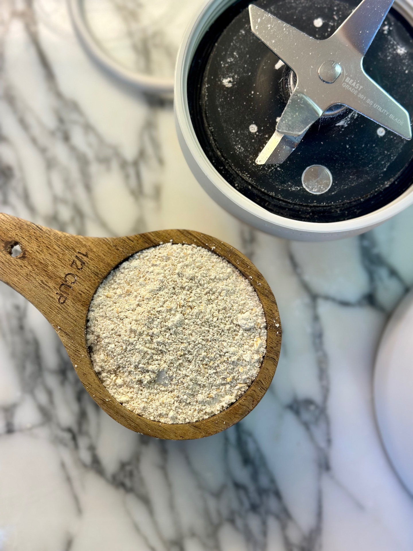 Blended oat flour in a wooden measuring cup beside the blender
