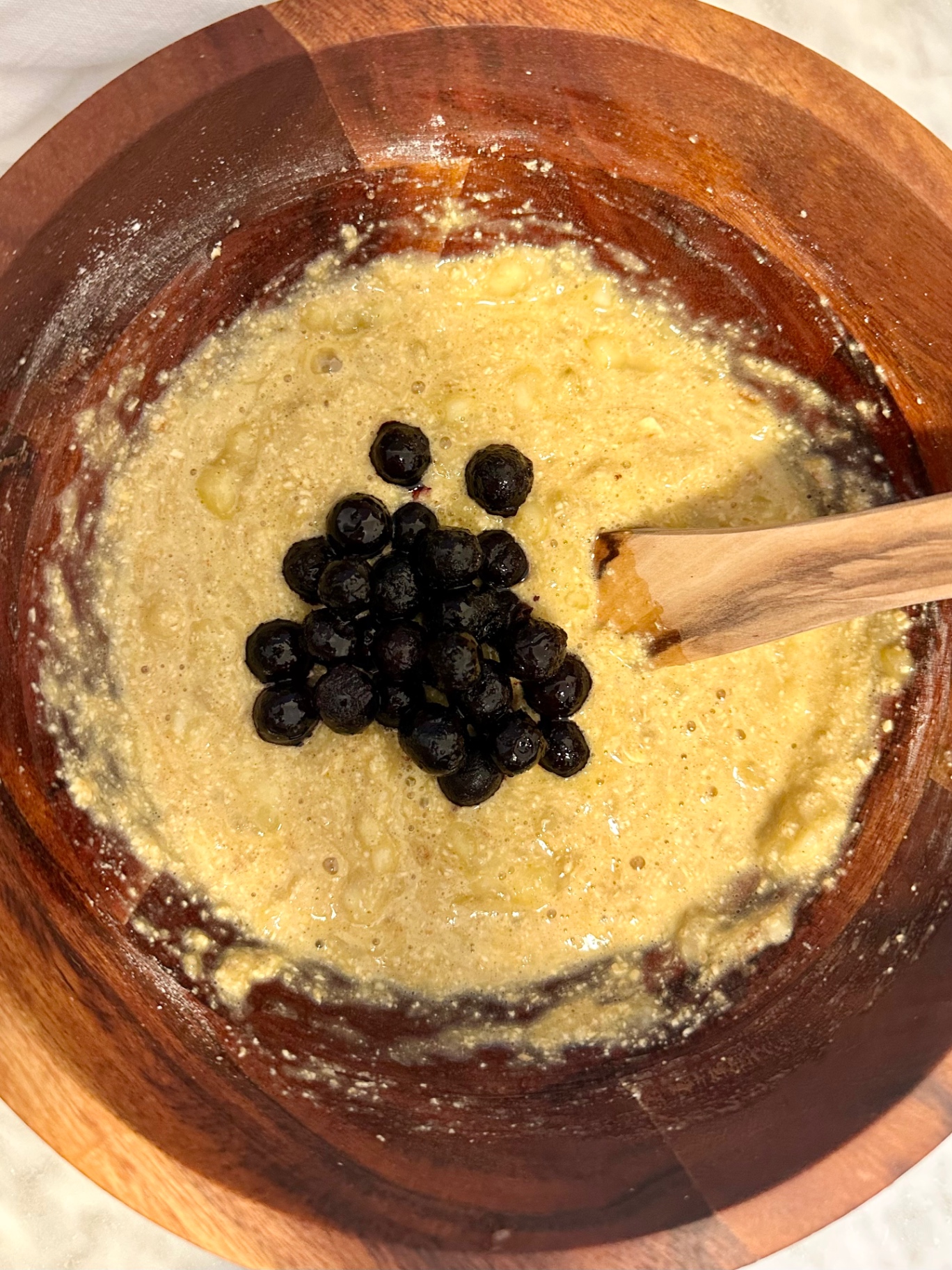 Frozen blueberries added to pancake batter in a wooden bowl