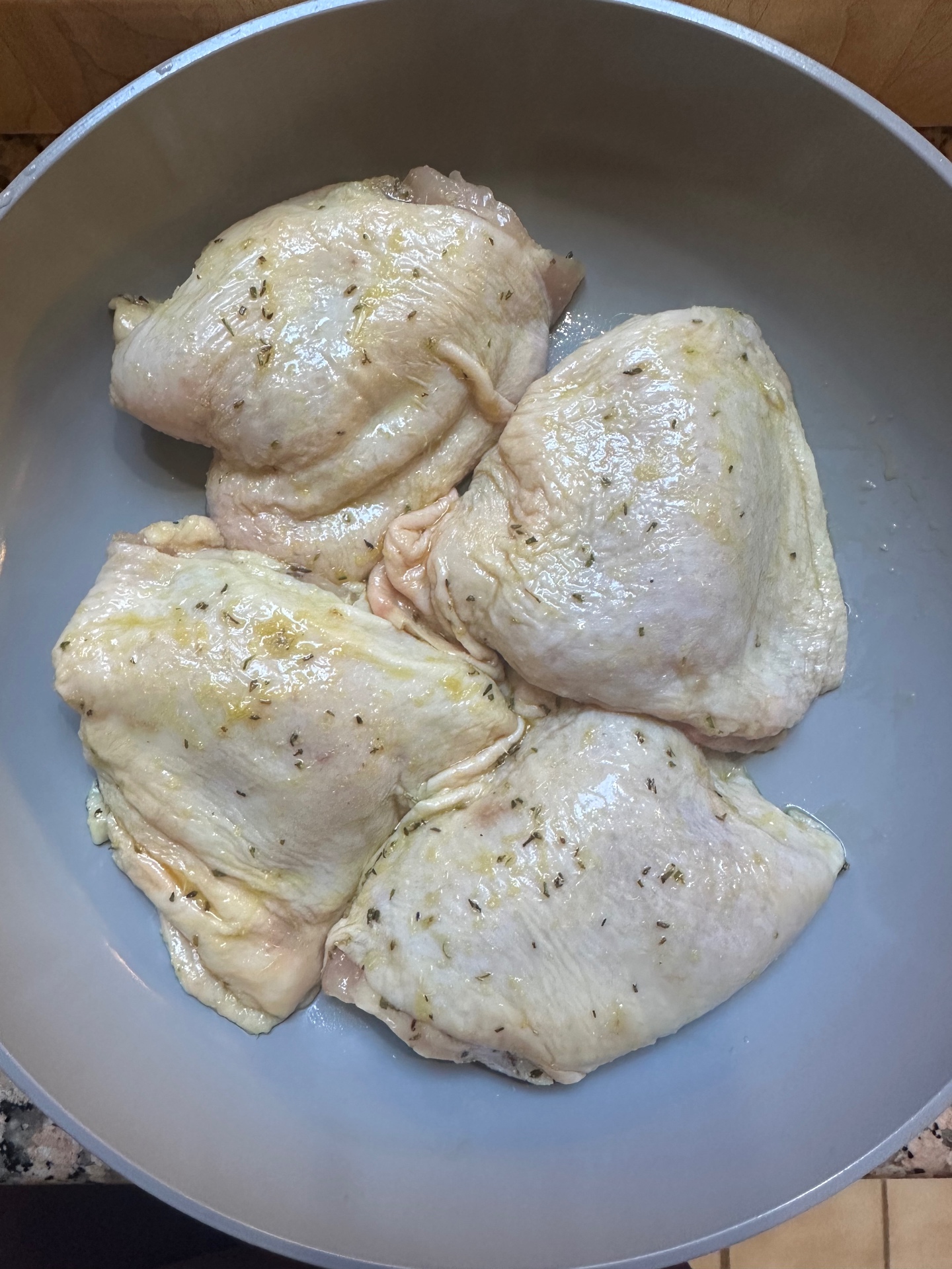 Raw bone in chicken pieces coated in oil and dried herbs in a grey pan