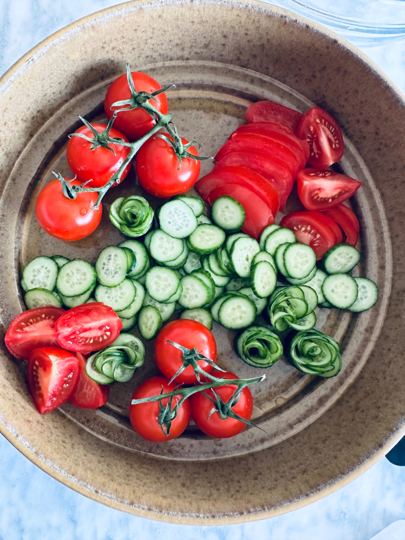 The salad nearly arranged in the bowl with tomato slices, cucumber rounds, and rosettes