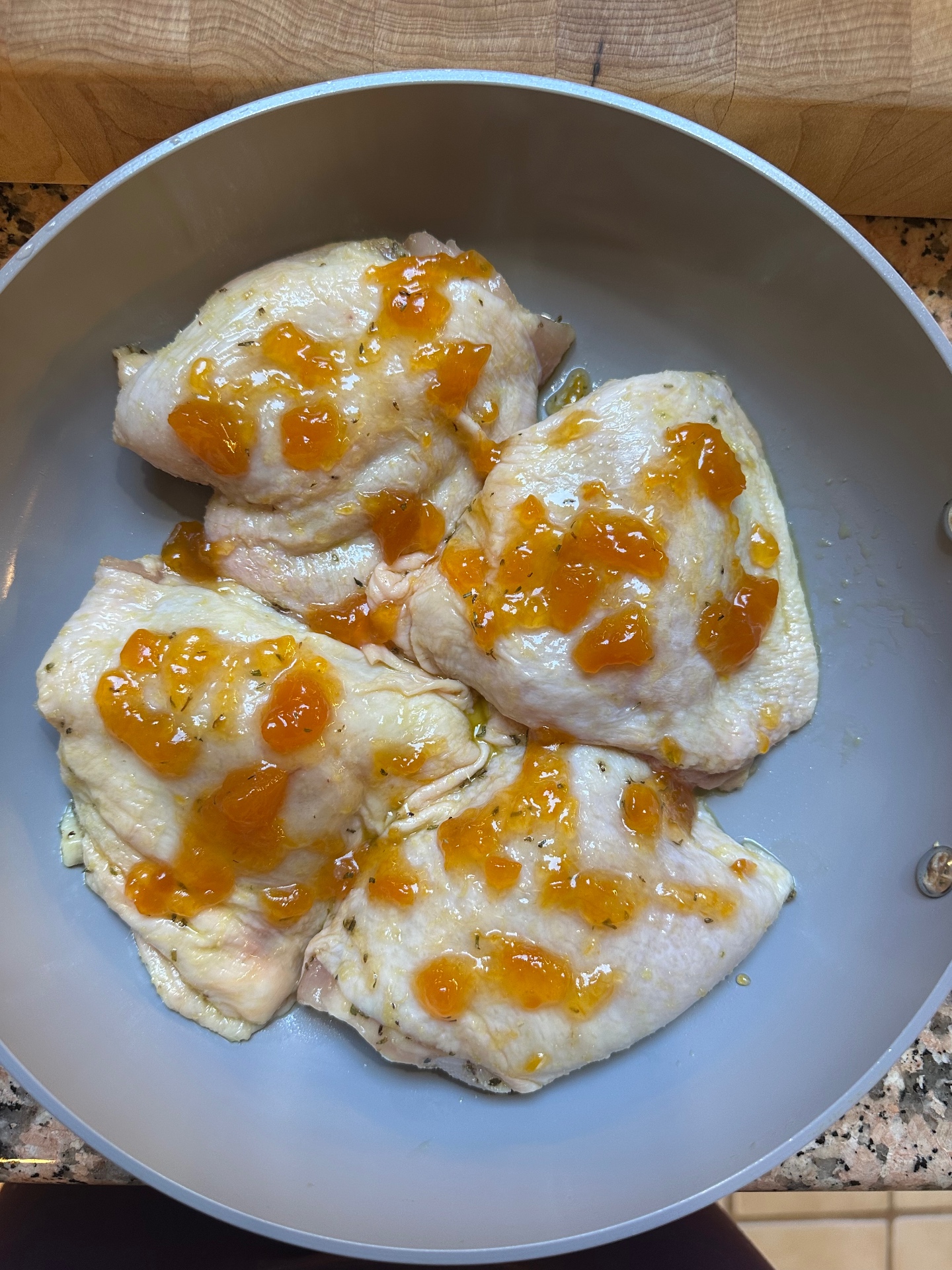 Raw chicken in a pan with dollops of orange marmalade scattered over the top