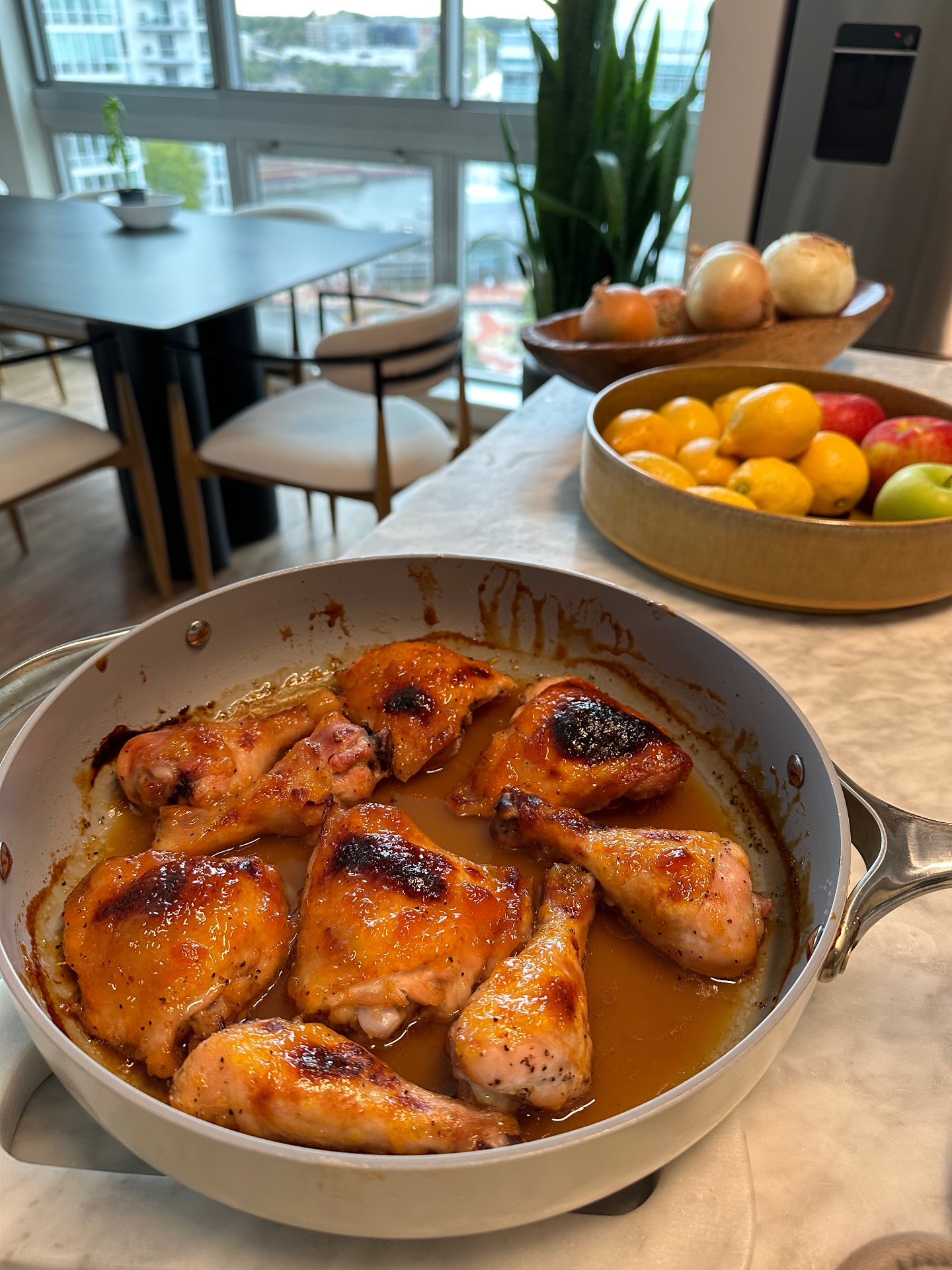 Finished marmalade chicken in a pan on a marble counter beside a bowl of lemons and apples